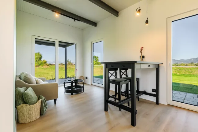 Heller Wohnraum des Tiny Houses mit Bartisch, Sessel und Terrassentüren